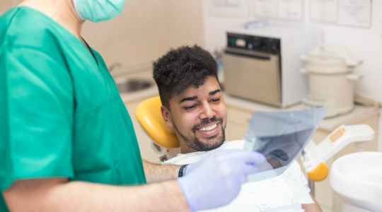 A dental clinician shows a photo to a patient who is sat in the dentist chair